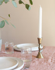 Table setting with plates, glasses, a candle in a brass holder, and greenery on a neutral background.