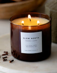 Lit candle in a glass jar with 'Slow North' label on a marble surface