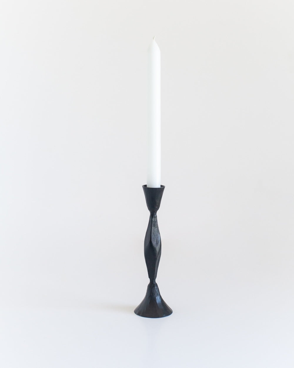 A single hand-forged iron candle holder with a diamond pattern design, standing upright against a white background with a candle on top of it