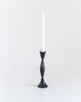 A single hand-forged iron candle holder with a diamond pattern design, standing upright against a white background with a candle on top of it