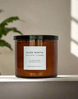 Candle with 'Slow North' label on a surface with a plant and light in the background