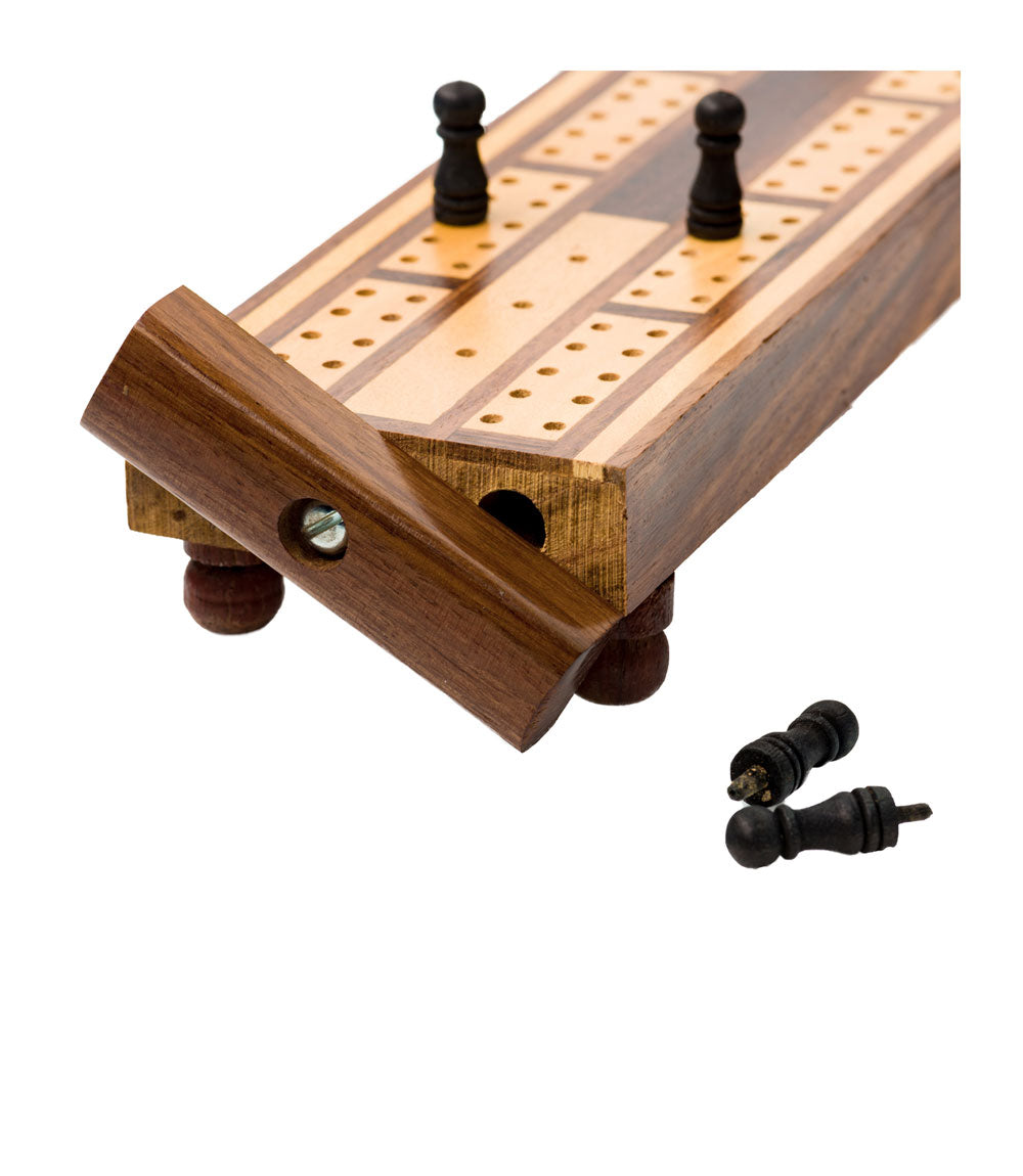 An up close view of a traditional wooden cribbage board with carved-out storage for game pieces, featuring a patterned design with black and gold elements.