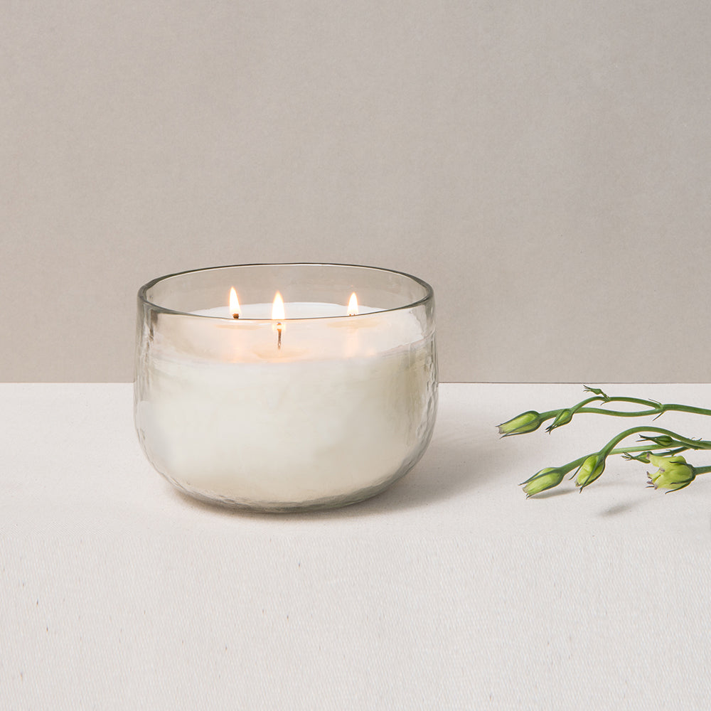 Glass candle with two flames on a white surface with a light beige background
