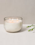 Glass candle with two flames on a white surface with a light beige background