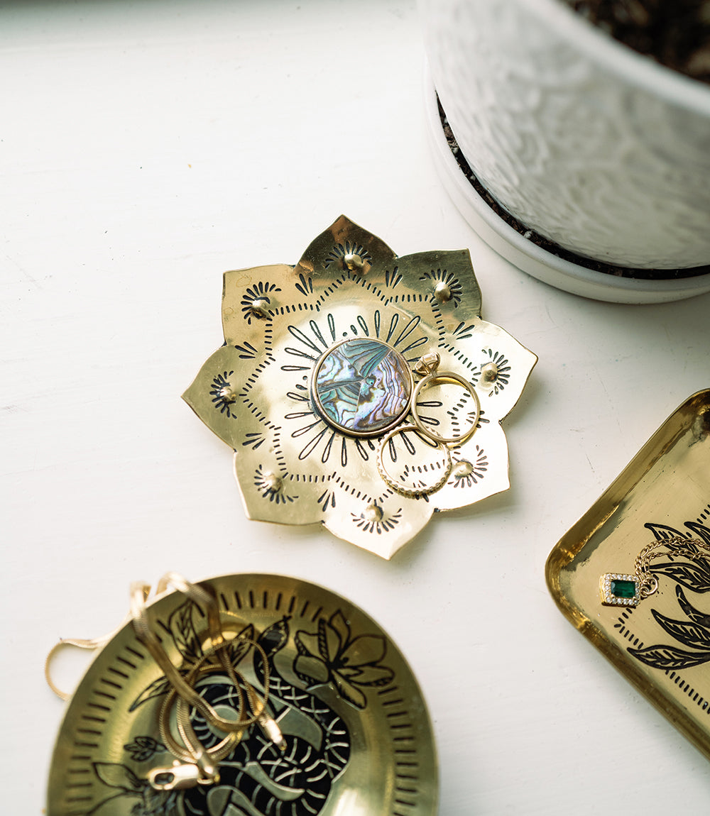A brass tray with a lotus design and an inlaid abalone center holding rings on top of a table