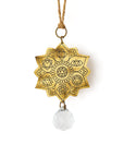 A brass suncatcher with a engraved lotus flower design and a glass bead pendant hanging from a cord