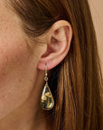 Teardrop-shaped earring with floral design worn by a person with brown hair.