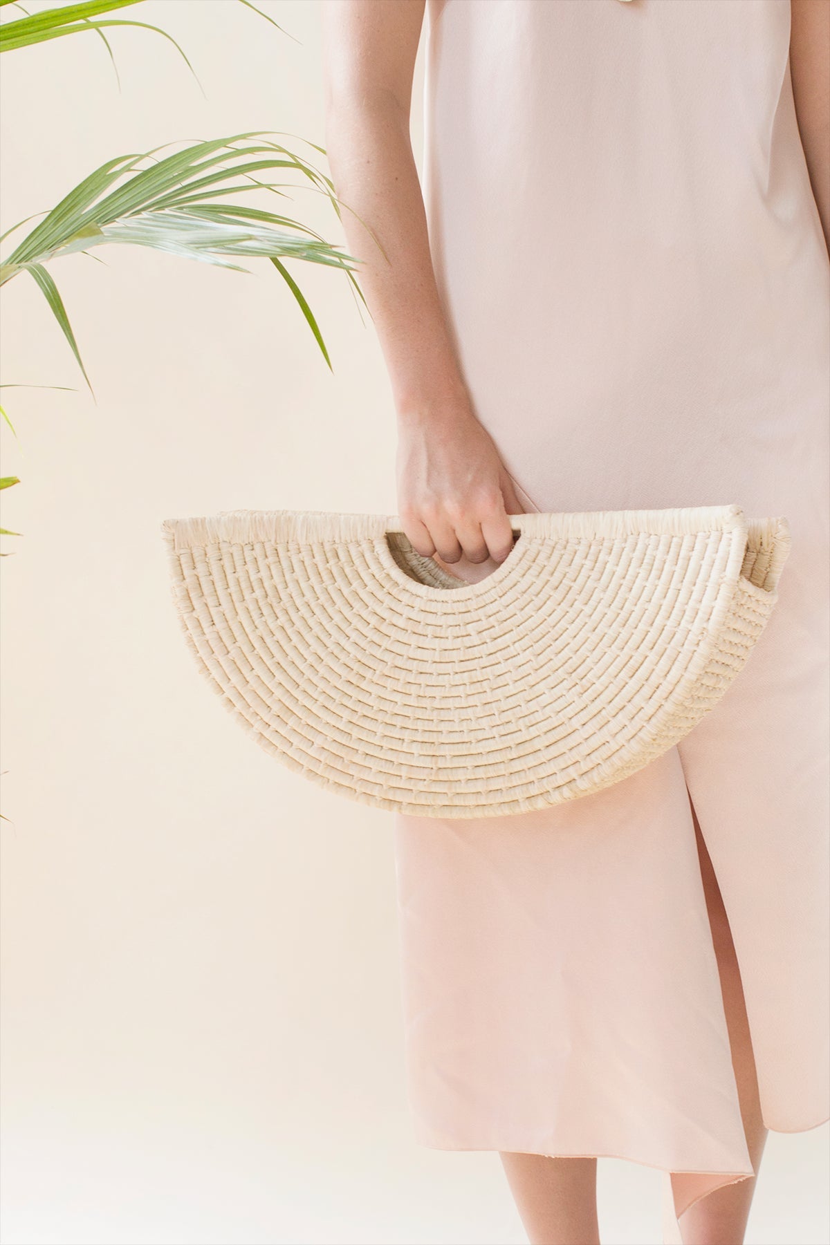 A woman carrying a beige, geometric, shell-shaped hand tote bag made from woven raffia.