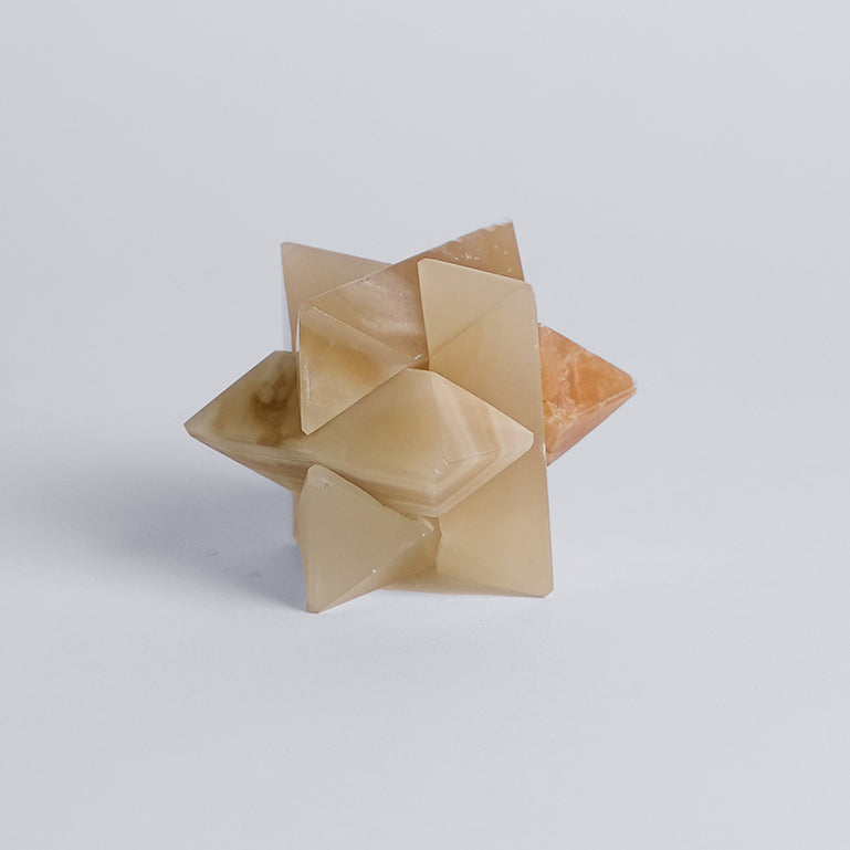 A creamy onyx burr star puzzle, with a complex star shape made from interlocking notched sticks, displayed on a white background.