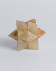 A creamy onyx burr star puzzle, with a complex star shape made from interlocking notched sticks, displayed on a white background.