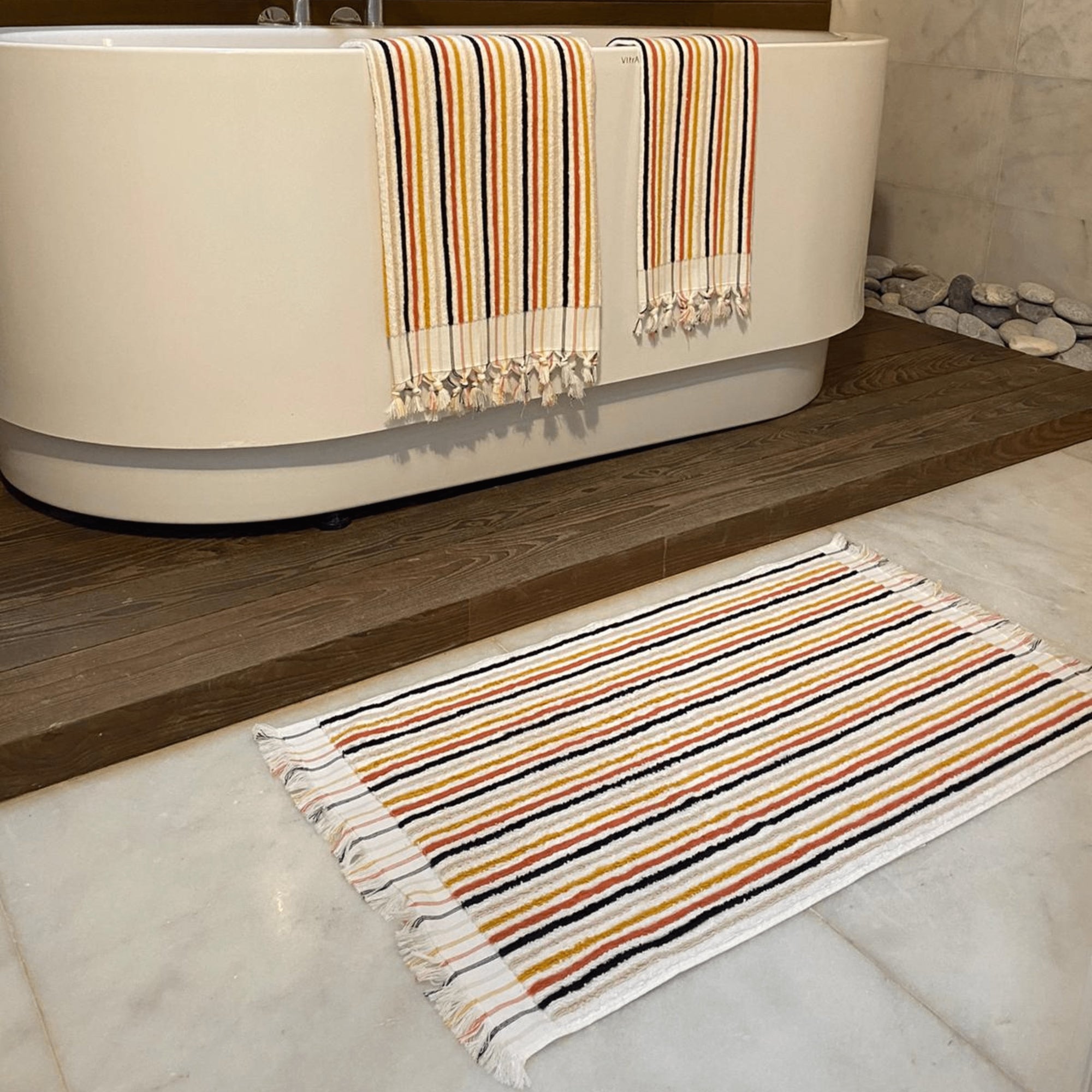 Striped bath mat in front of a bathtub with a striped towel draped over the edge