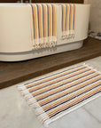 Striped bath mat in front of a bathtub with a striped towel draped over the edge