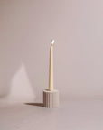 A natural sandstone taper candle holder with a lit candle on it, against a neutral background.