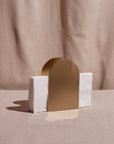 A stainless steel napkin holder with a brass finish, featuring a cylindrical holder with a flat base, containing a white napkin