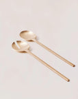 A pair of brass salad servers with a sleek design, laid out on a light background