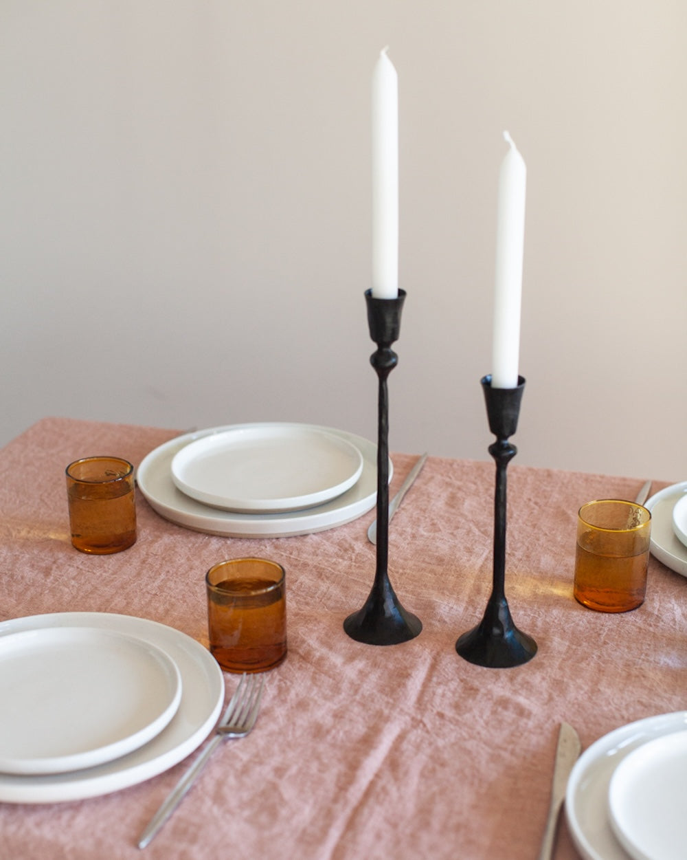 Dining table setting with white plates, brown glasses, and black candlesticks.