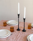 Dining table setting with white plates, brown glasses, and black candlesticks.