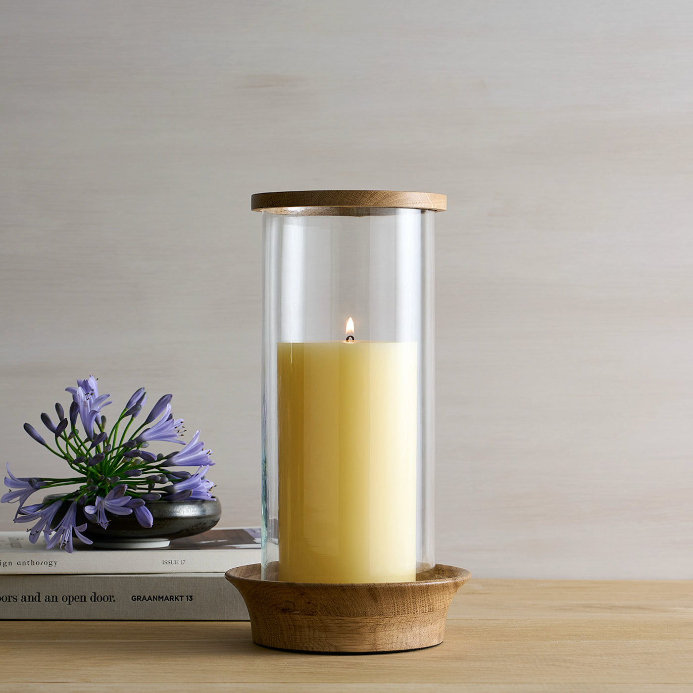 Candle in a glass holder with wooden base on a table with a minimal background