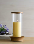Candle in a glass holder with wooden base on a table with a minimal background