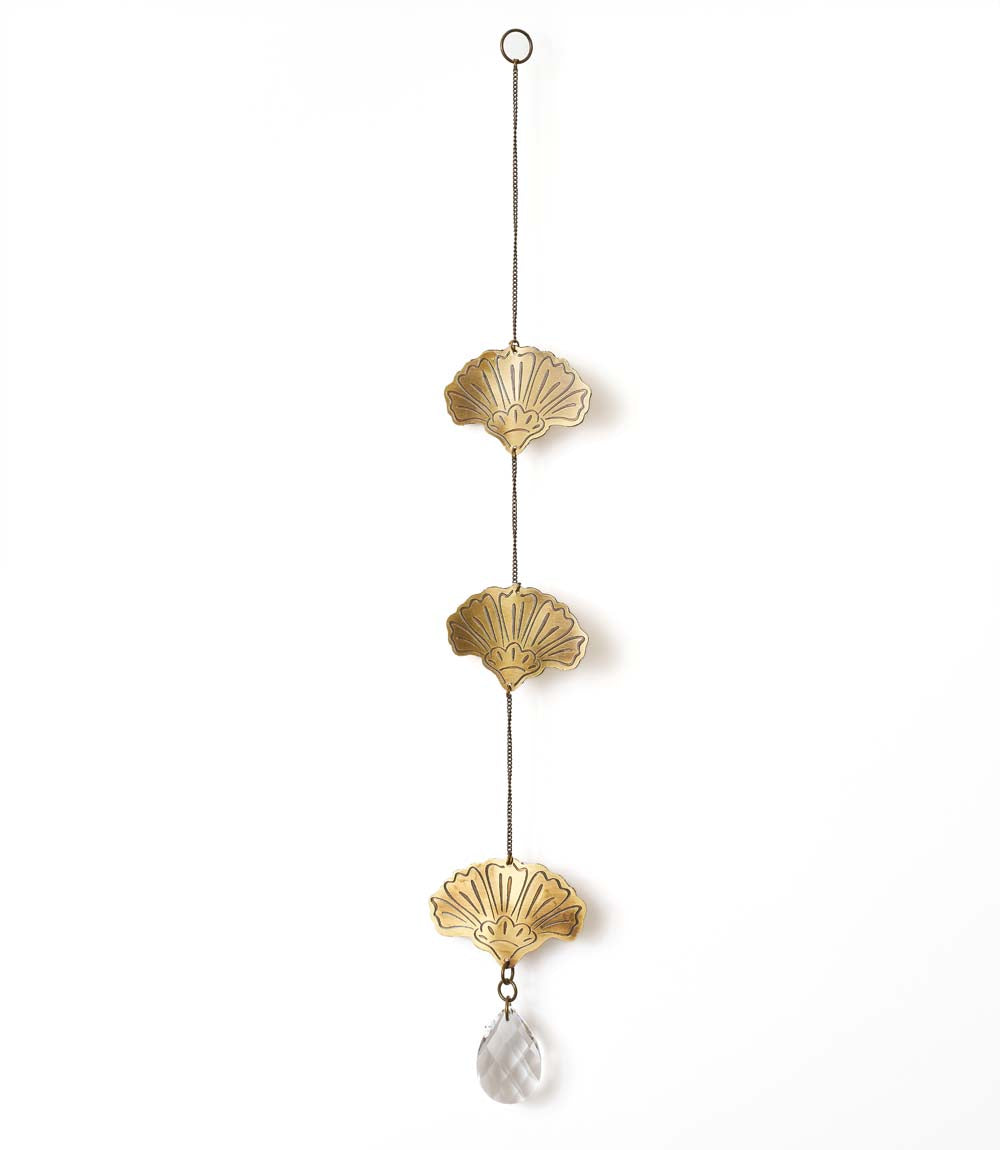 A brass suncatcher with engraved ginkgo leaf motifs and a glass bead, hanging from a metal loop.