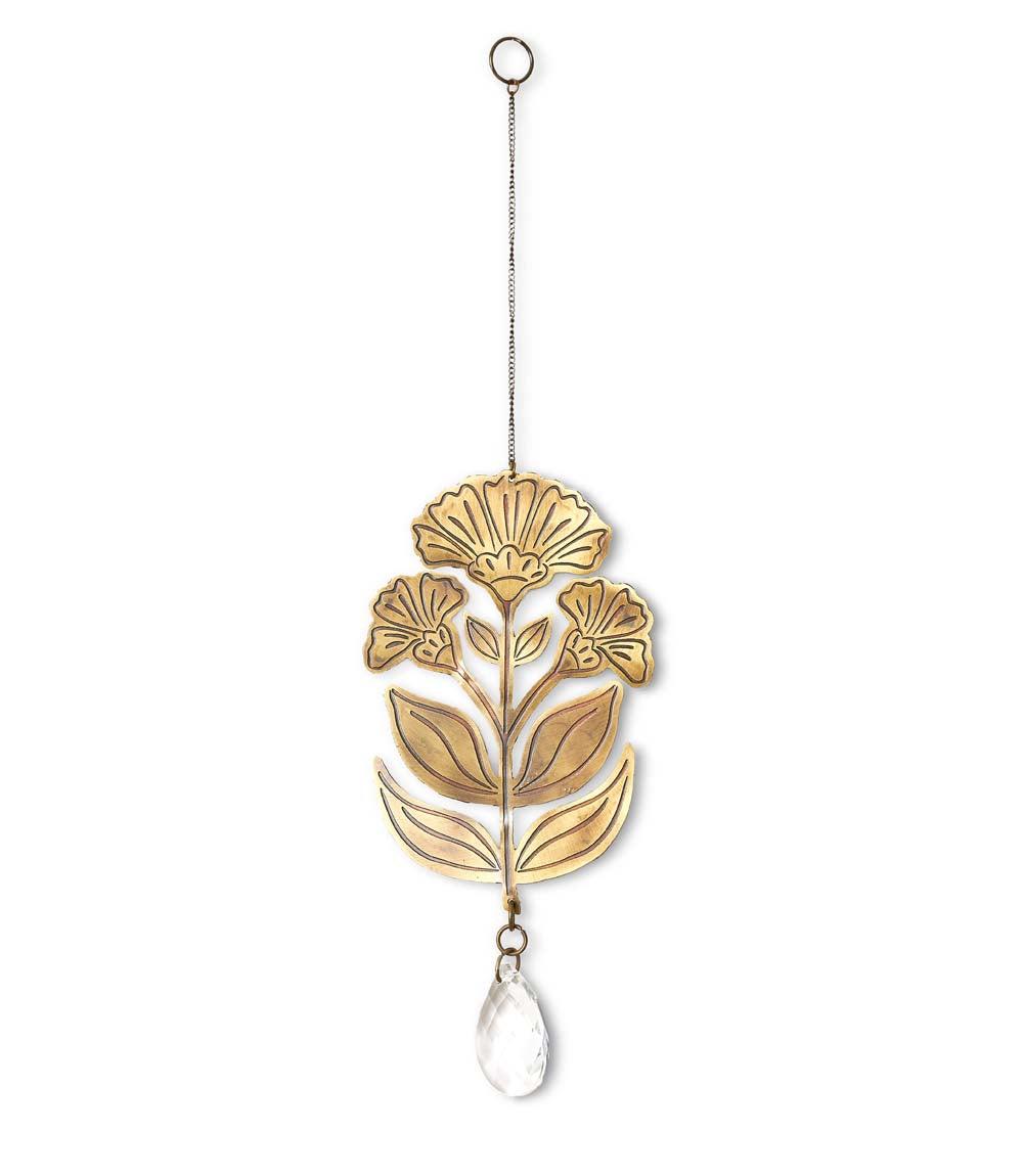 A brass suncatcher with an embossed flower design and a teardrop crystal pendant, hanging from a cord.