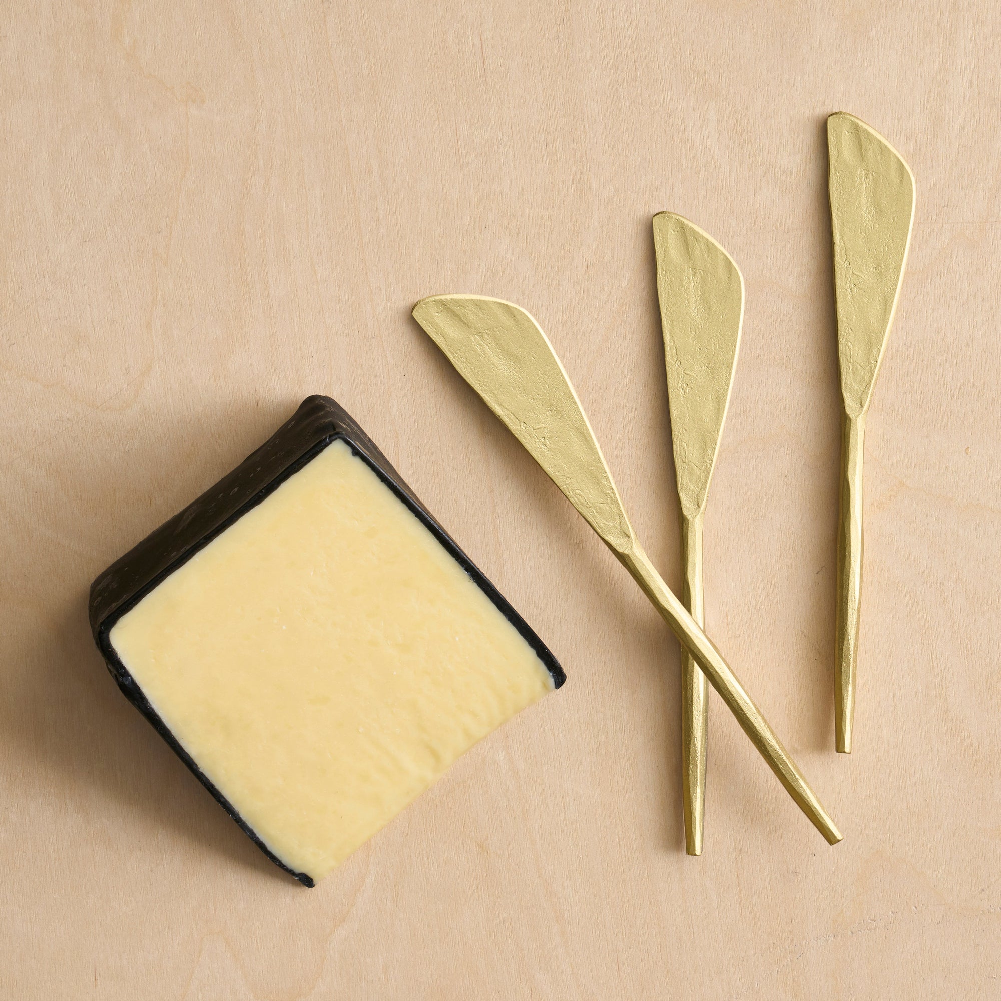 Block of butter with three gold butter knives on a beige background