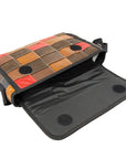 A crossbody bag with a patchwork design made from upcycled leather, featuring a black nylon strap and interior pockets, in brown, red, and blue colors with the flap closure open.