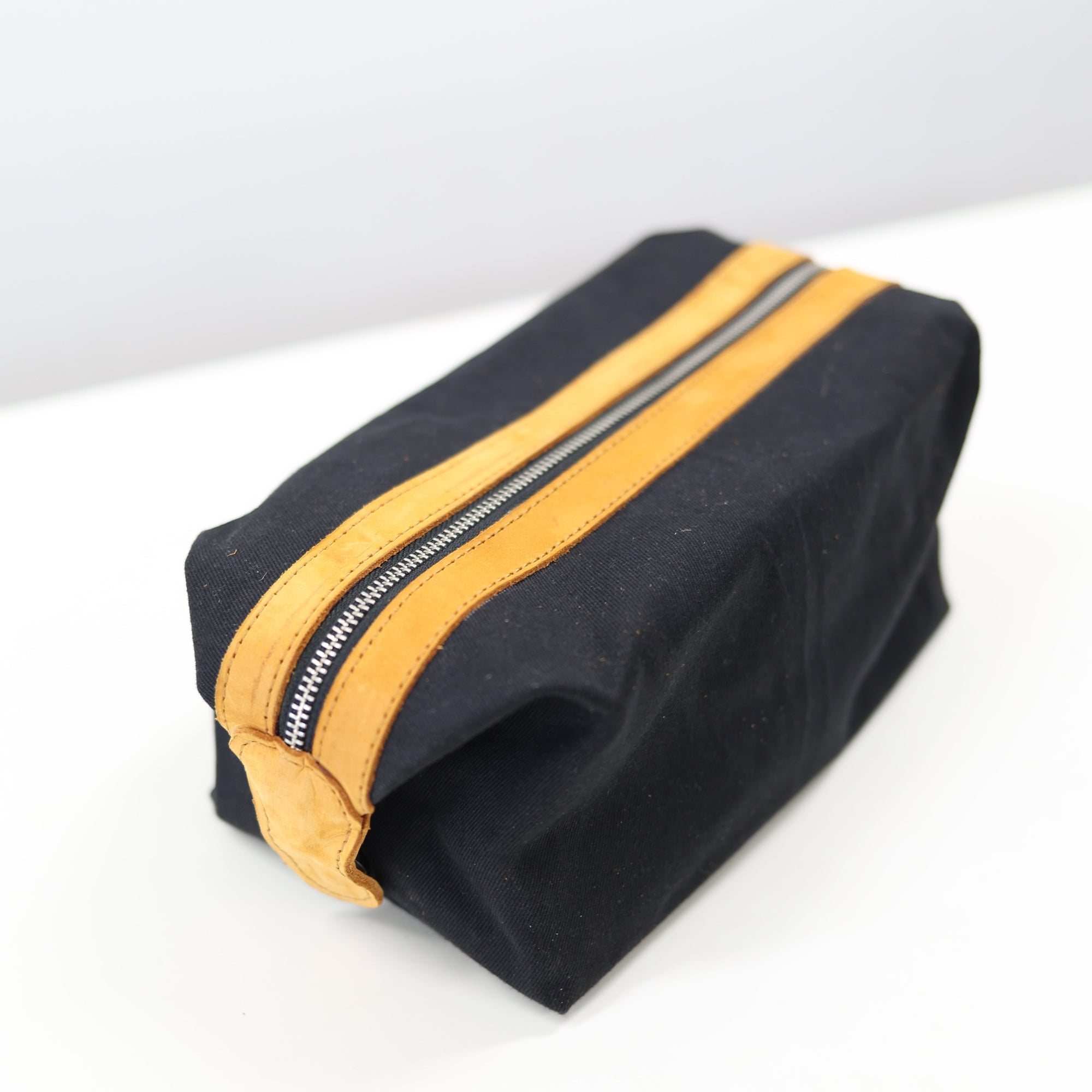 A black toiletry bag with a yellow zipper and leather details on a white background.