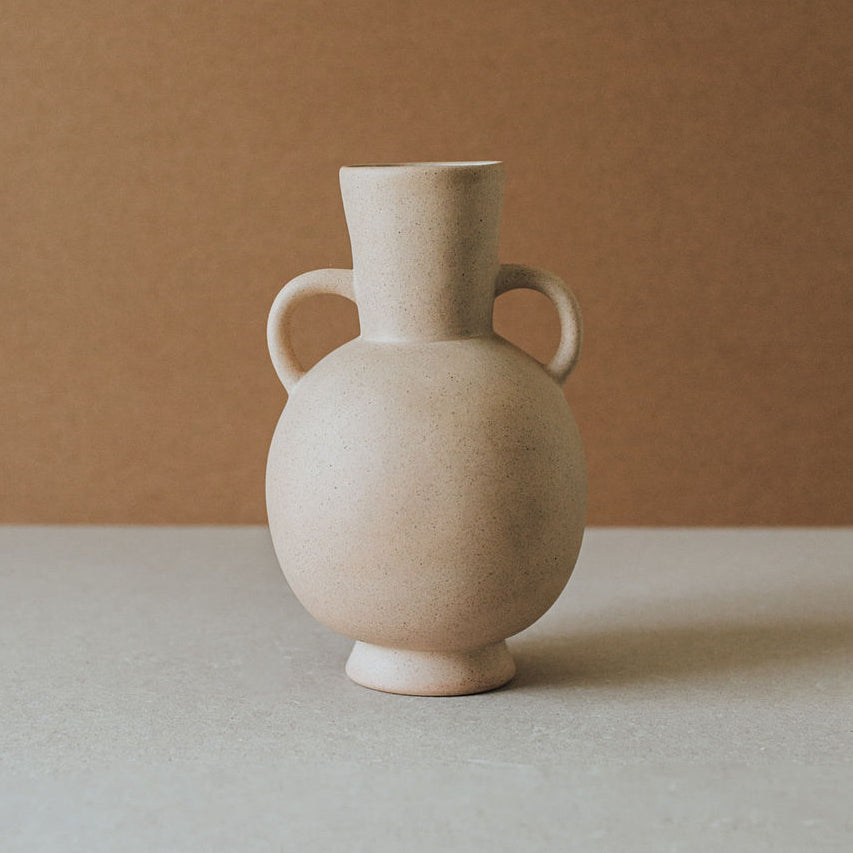 A beige ceramic vase with two handles, a rounded body, and a narrow neck, placed against a neutral background.