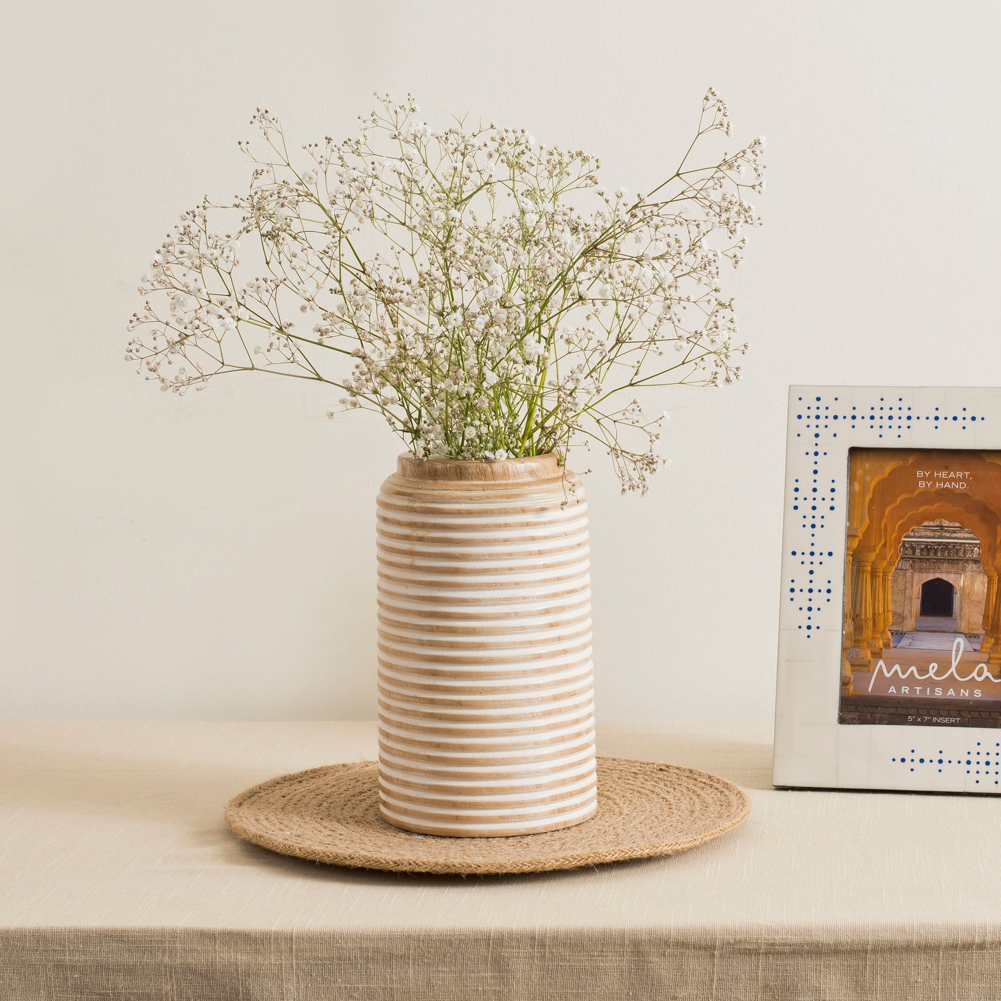 A wooden cylindrical vase with a rustic red and white design and etched lines with plants inside on a table