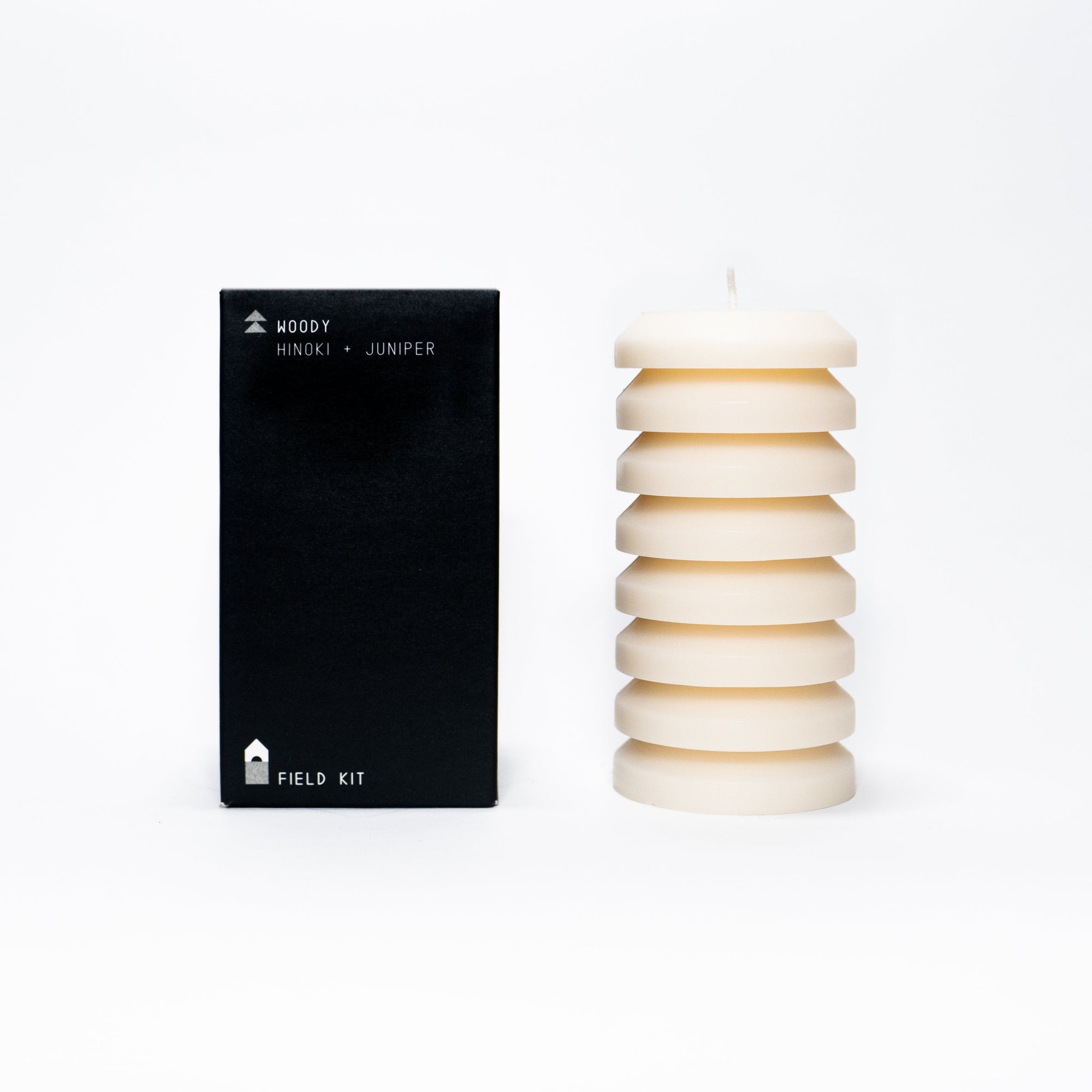 A sculptural pillar candle designed for burning, shown alongside its packaging which indicates the scent of hinoki, juniper, and black spruce.