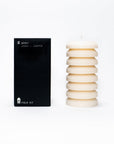A sculptural pillar candle designed for burning, shown alongside its packaging which indicates the scent of hinoki, juniper, and black spruce.