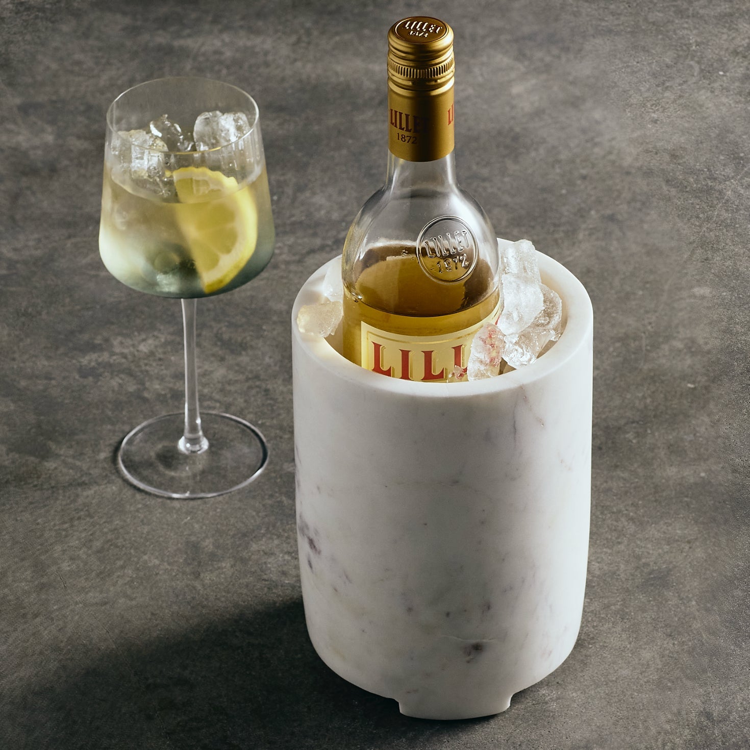 Bottle of Lillet in a marble cooler with a glass of lemonade on a gray surface