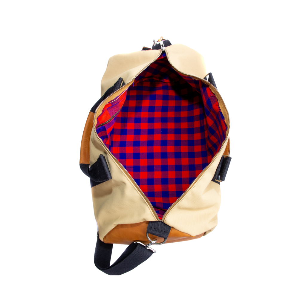 The inside of a beige and brown duffel bag with black straps and a tan leather bottom, standing upright on a plain background.