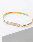 Gold bracelet with a bar design featuring a white pearl on a light gray background
