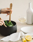 Hands scooping salad out of a a hand-crafted stoneware bowl with a black color
