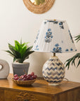 Decorative lampshade with floral pattern on a wooden table with books and a plant.