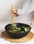 Two olive wood spatulas being held by hands scooping a salad