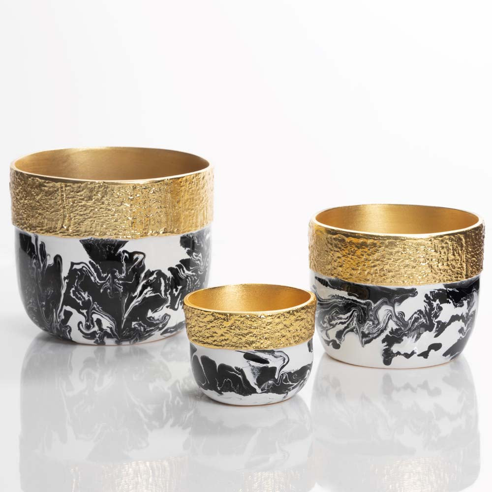 Three decorative cups with gold rims and black and white marbled patterns on a reflective surface.