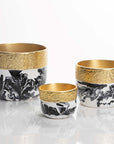 Three decorative cups with gold rims and black and white marbled patterns on a reflective surface.