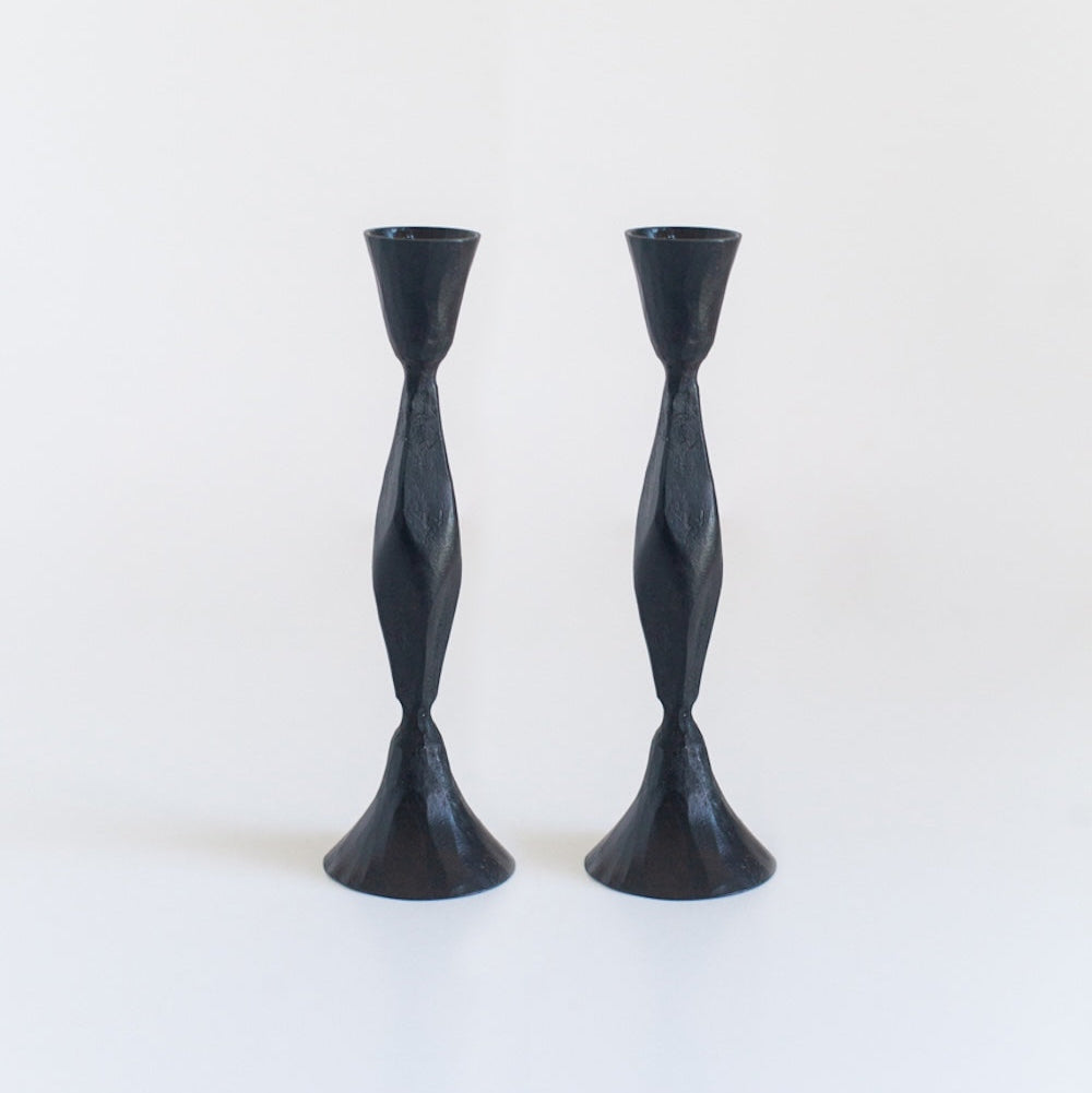 A pair of black, hand-forged iron candle holders with a diamond pattern design, standing upright against a white background.