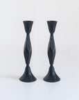 A pair of black, hand-forged iron candle holders with a diamond pattern design, standing upright against a white background.