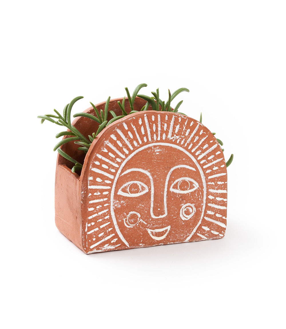 A terracotta planter with a hand-painted sunrise design in white, featuring a smiling sun face