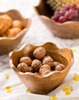 Wooden bowl filled with walnuts on a floral tablecloth with other bowls of fruits in the background