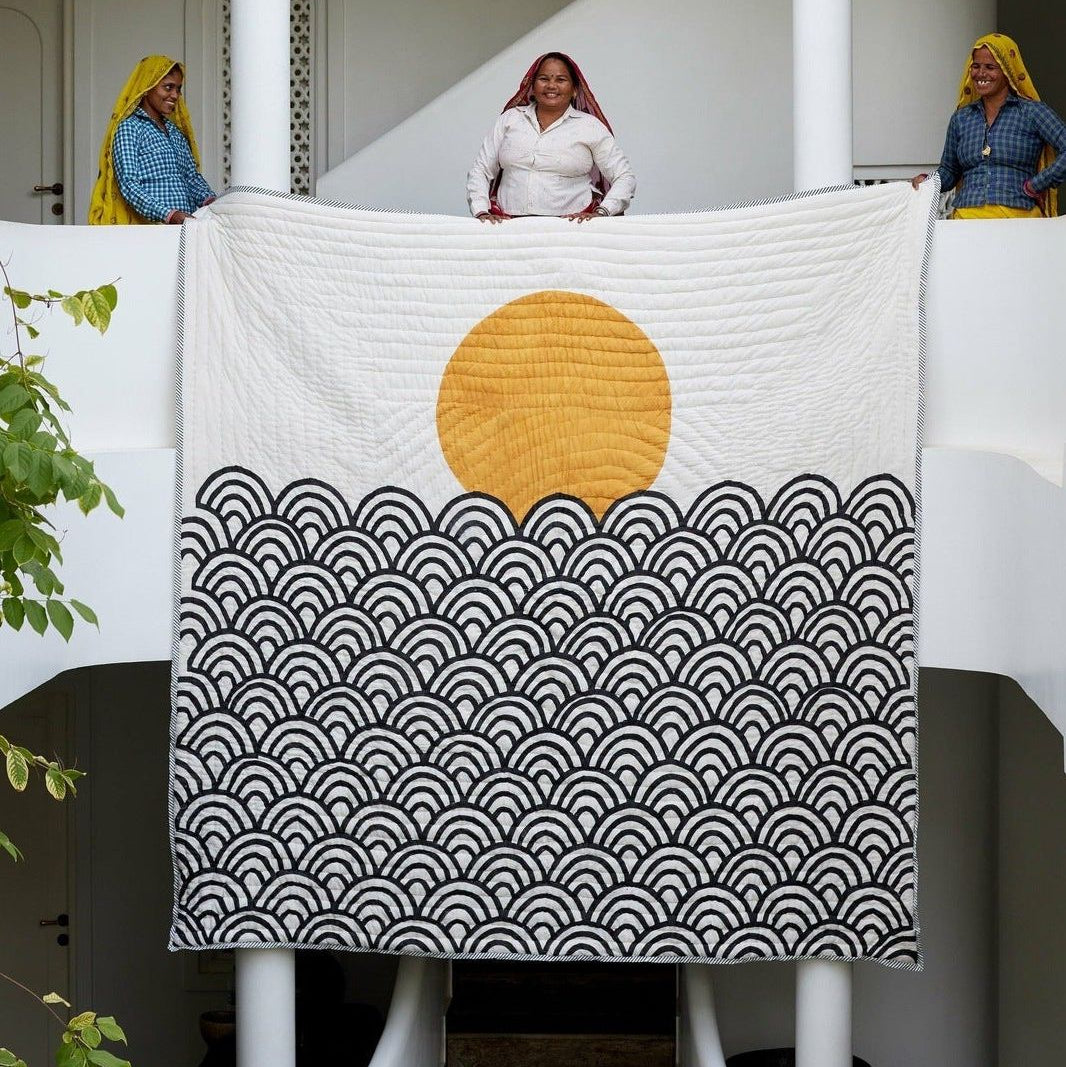 Quilt with a sun and waves design being held by artisans