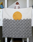 Quilt with a sun and waves design being held by artisans