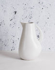 A white stoneware pitcher with a handle on the side and a smooth, rounded body