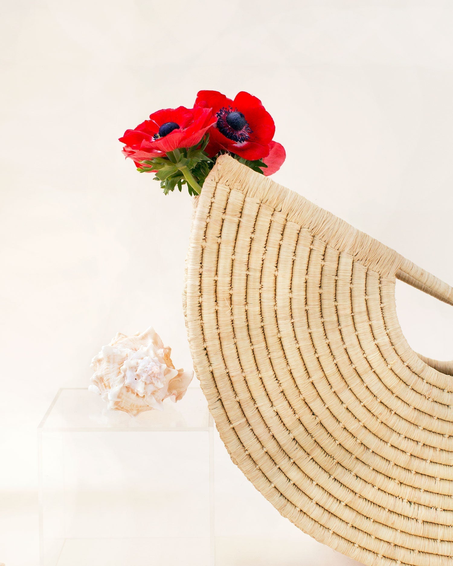 A zoomed in picture of a beige, geometric, shell-shaped hand tote bag made from woven raffia with a flower inside.