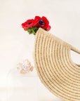 A zoomed in picture of a beige, geometric, shell-shaped hand tote bag made from woven raffia with a flower inside.