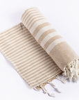 A rolled-up beige striped throw blanket with white stripes and fringes at the end, laid out on a white background